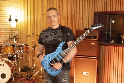 Un guitariste de Heartline pose avec une guitare électrique bleue dans un studio d’enregistrement.