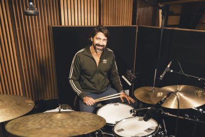 Un batteur d’Os Pariocas, baguettes en main, est installé derrière sa batterie au studio Midilive.