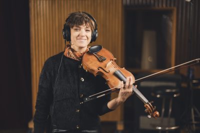 Une violoniste d’Os Pariocas, casque sur les oreilles, tient son violon au studio Midilive.