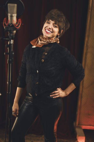 Une chanteuse d’Os Pariocas sourit près d’un microphone pendant la session au studio Midilive.