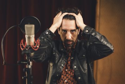 Un membre d’Os Pariocas pose les mains sur la tête devant un microphone au studio Midilive.