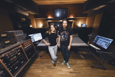 Deux membres de Jessie Lee & The Alchemists posent devant la console de mixage dans la régie du studio Midilive.